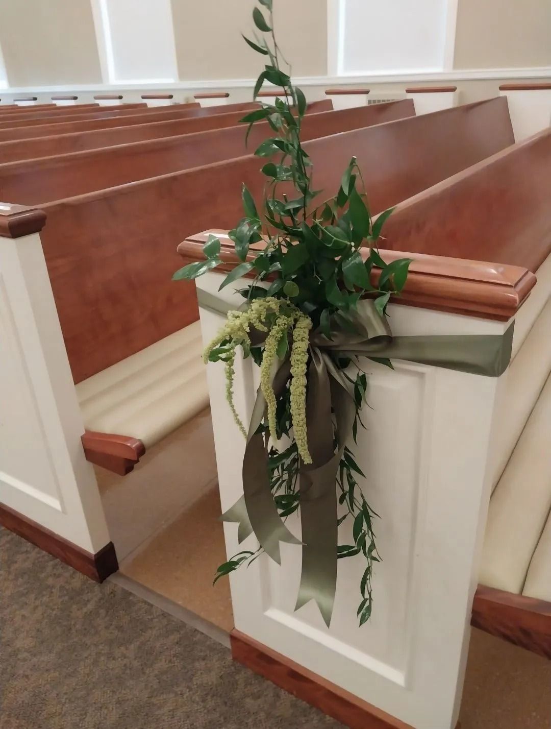 Floral arrangement of greenery and ribbons on church pew.