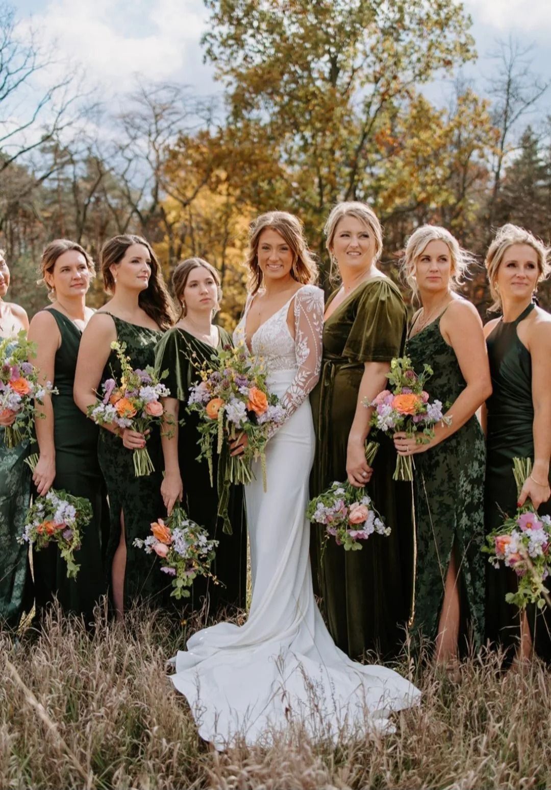 Bride with bridesmaids in green dresses, holding bouquets, standing outdoors.
