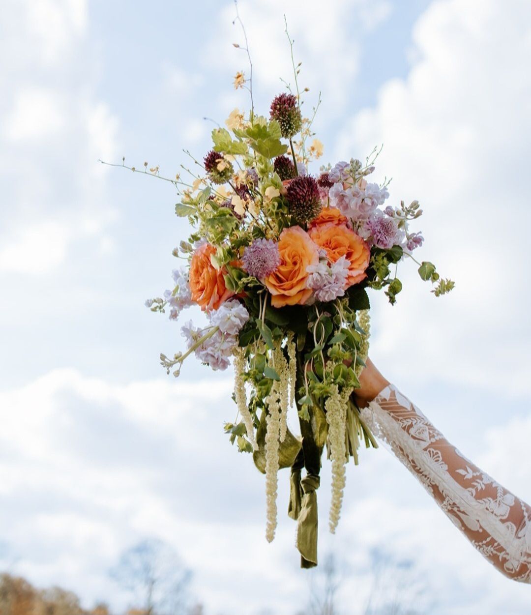Person holding a colorful bouquet of flowers against a cloudy sky.
