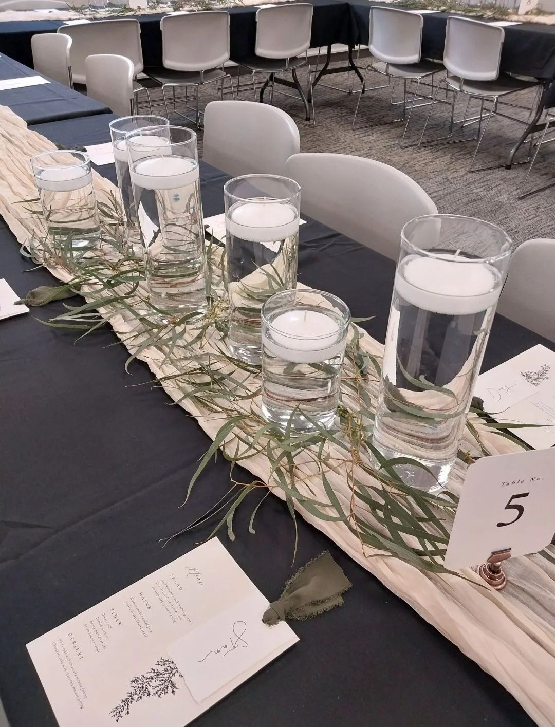 Table setting with tall vases, floating candles, greenery, and table number 5.