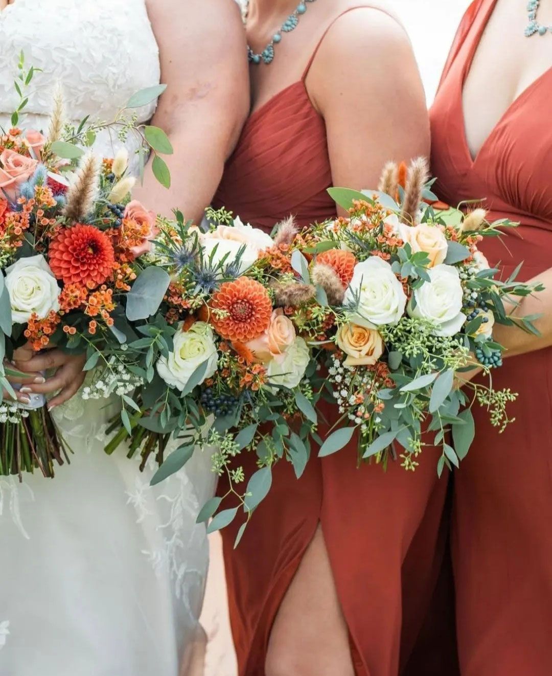 Bridesmaids in rust-colored dresses hold bouquets of orange, white, and green flowers.
