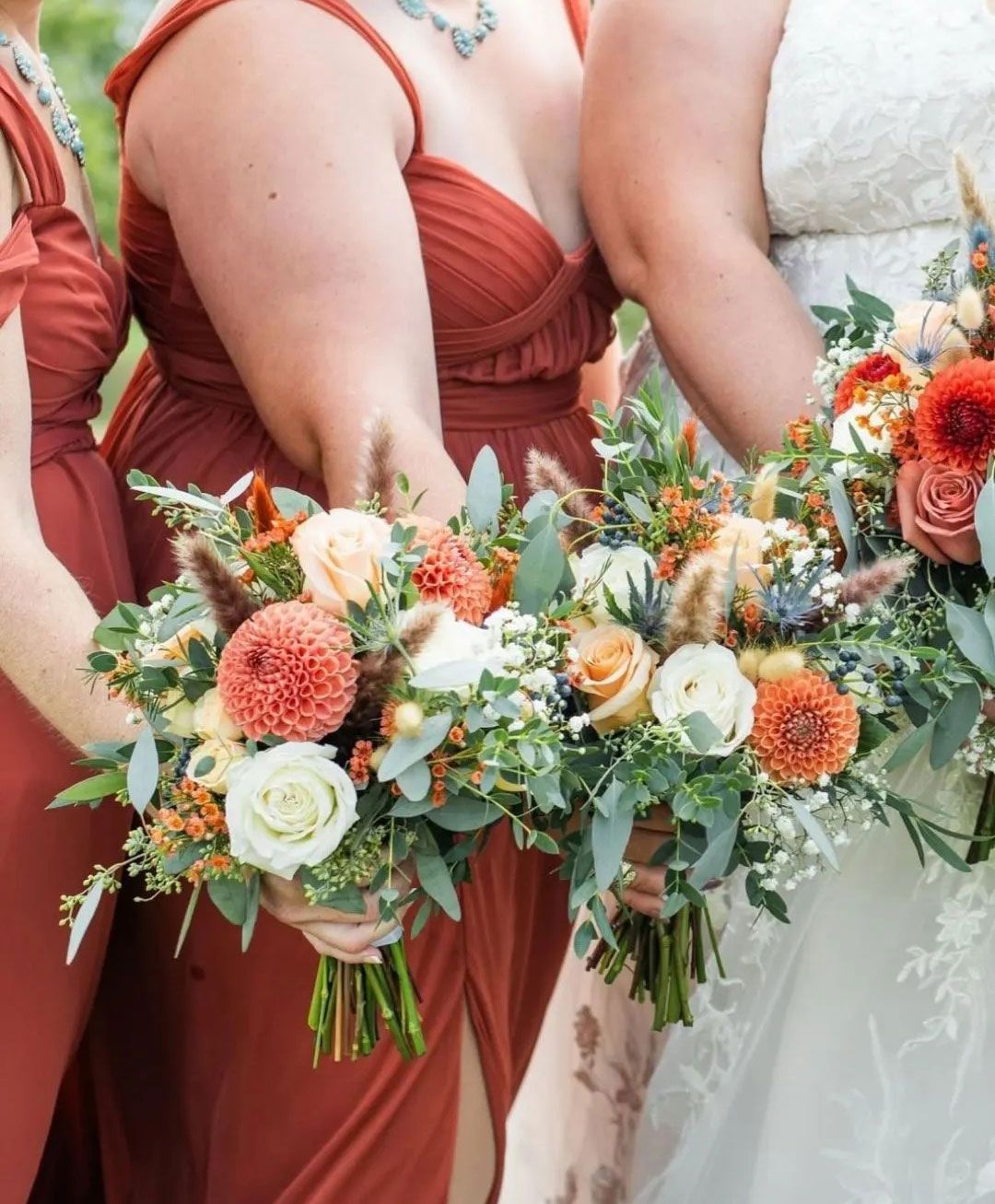 Bridesmaids in rust dresses holding bouquets of orange, cream, and green flowers.