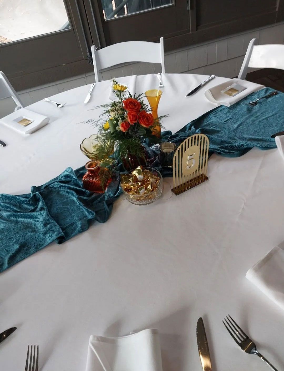 Round table set for dining with turquoise runner, floral centerpiece, and place settings.