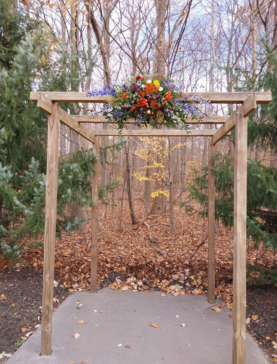 Wooden arch decorated with colorful flowers in a wooded setting.