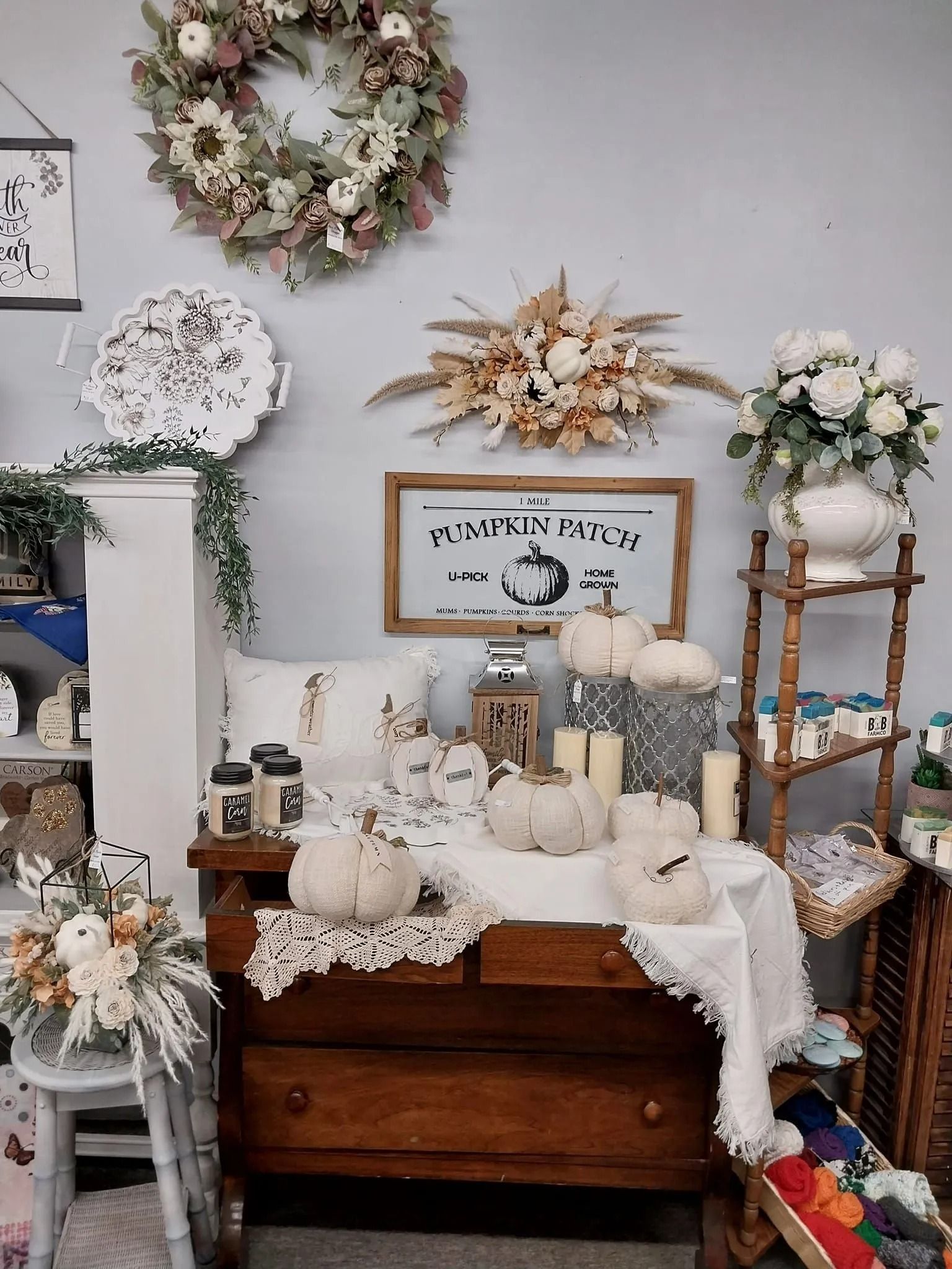 Fall-themed display featuring pumpkins, a wreath, floral arrangements, candles, and a