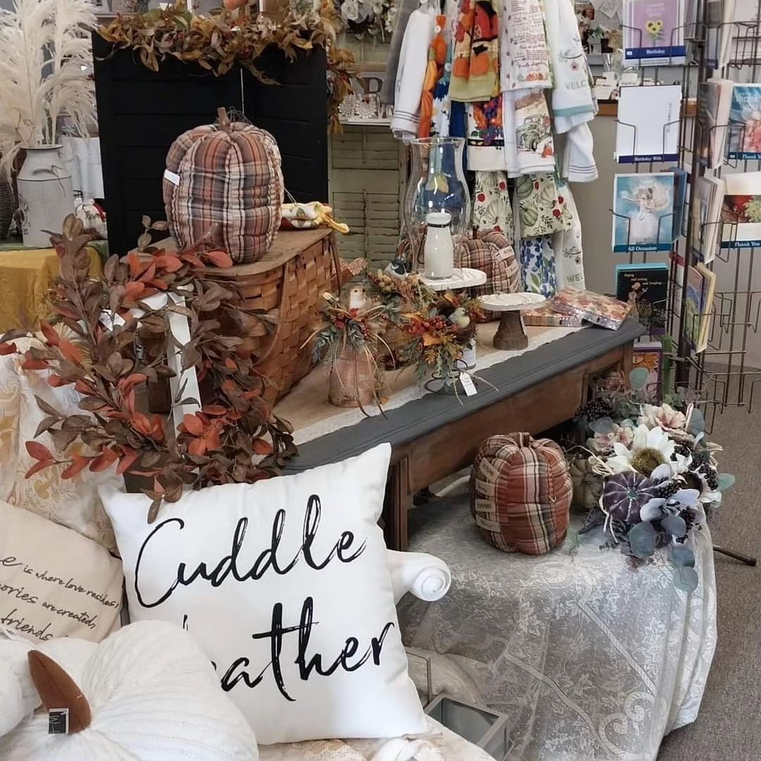 Fall-themed store display with plaid pumpkins, pillows, floral arrangements, and decorative towels.