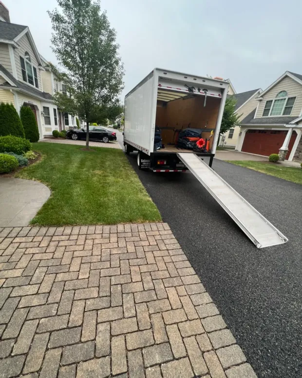 White moving truck with ramp extended on a residential street.