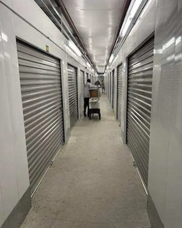 Storage unit hallway with metal doors. Person with a cart moves boxes down the aisle.