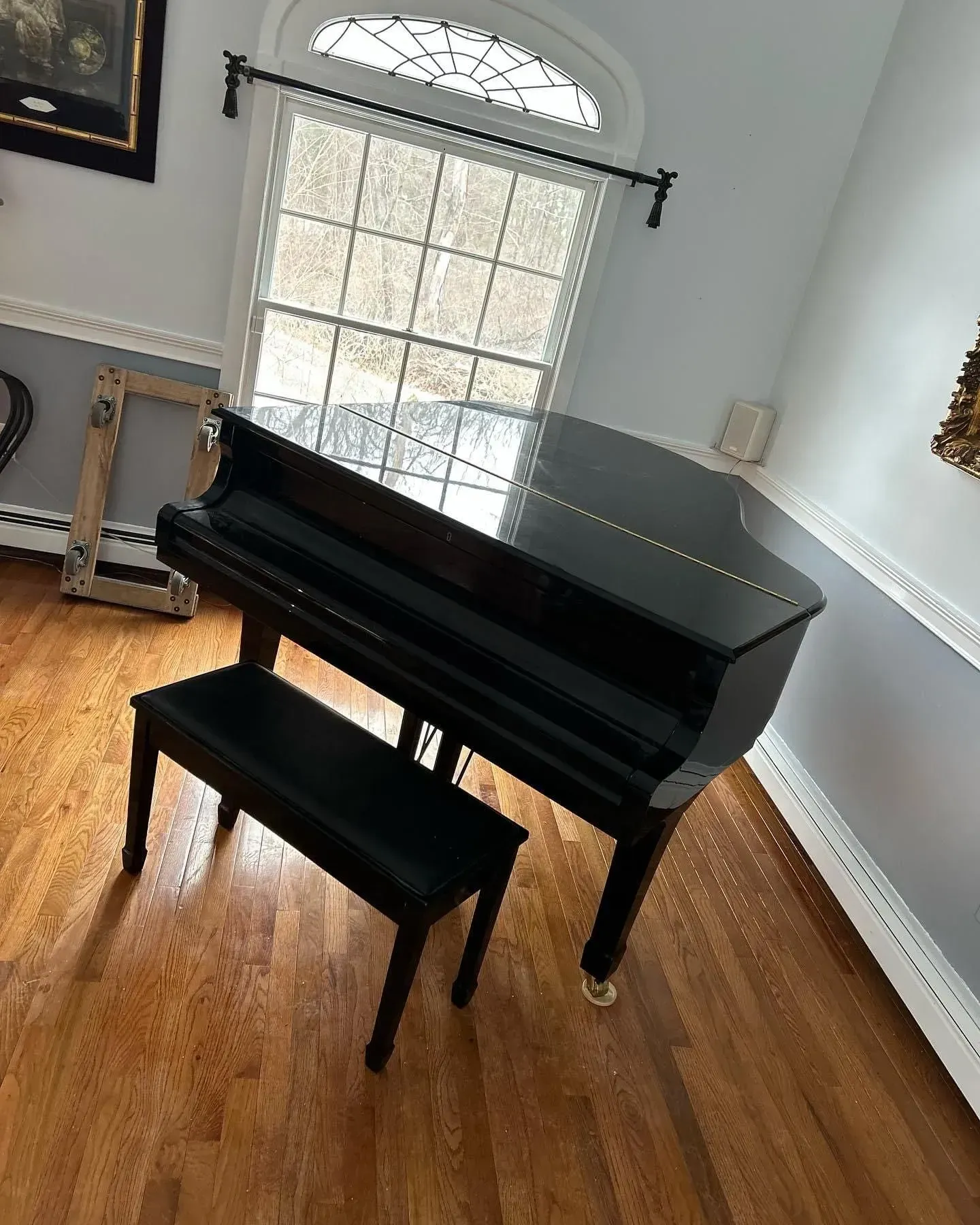 Black grand piano with a bench on a hardwood floor, near a window.