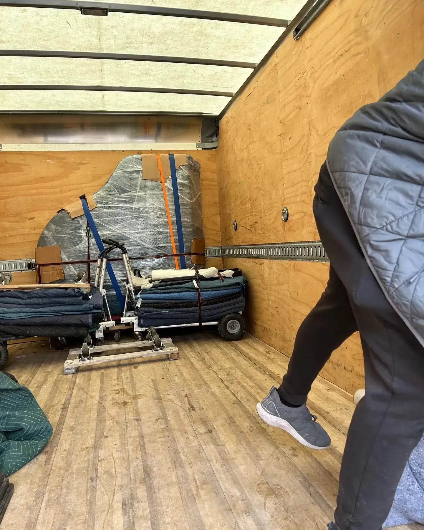 Inside a moving truck; a person, side view, enters frame. Carpeting and wrapped items are inside the truck.
