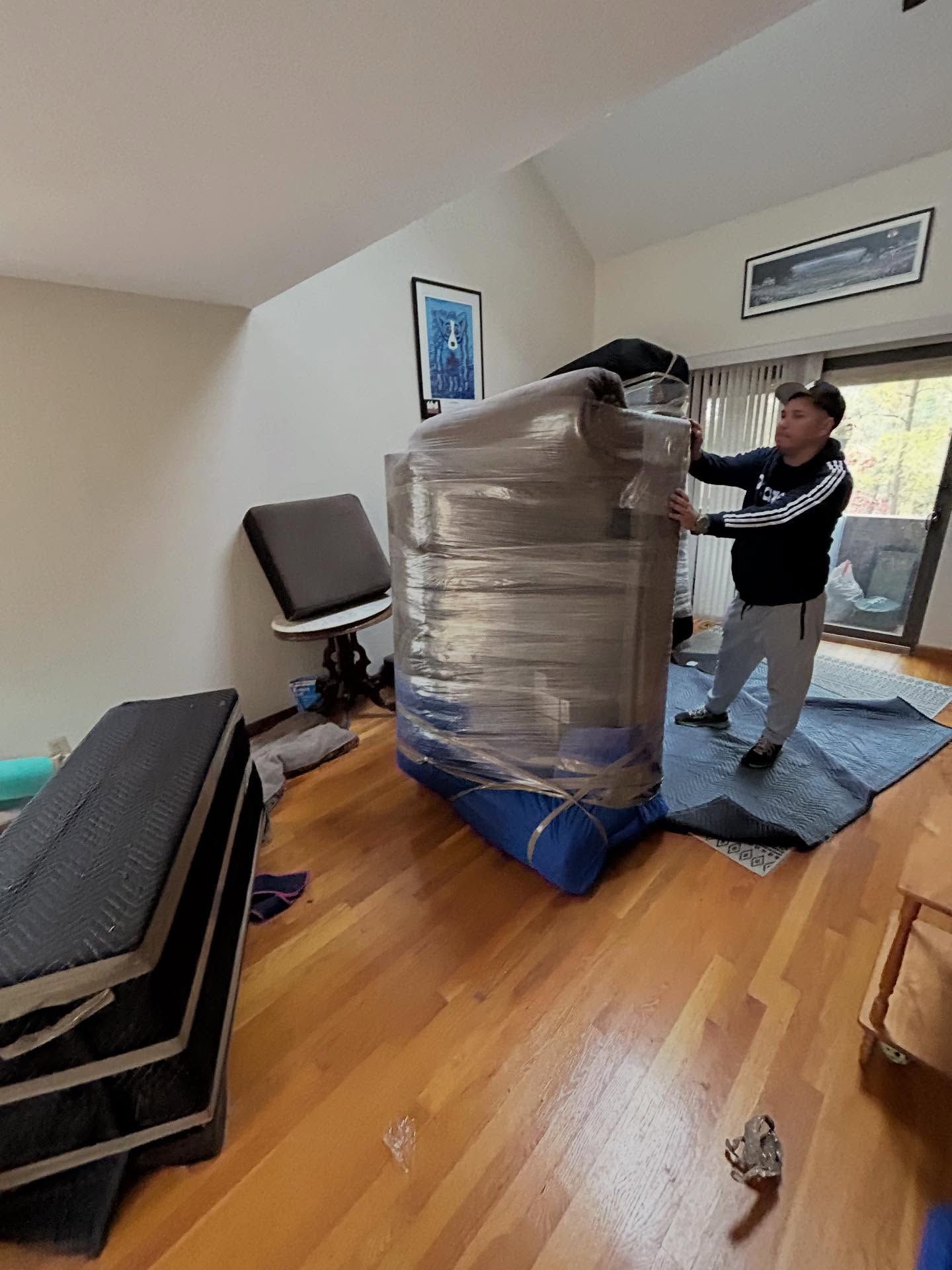 Man wrapping furniture in clear plastic in a room with hardwood floors.