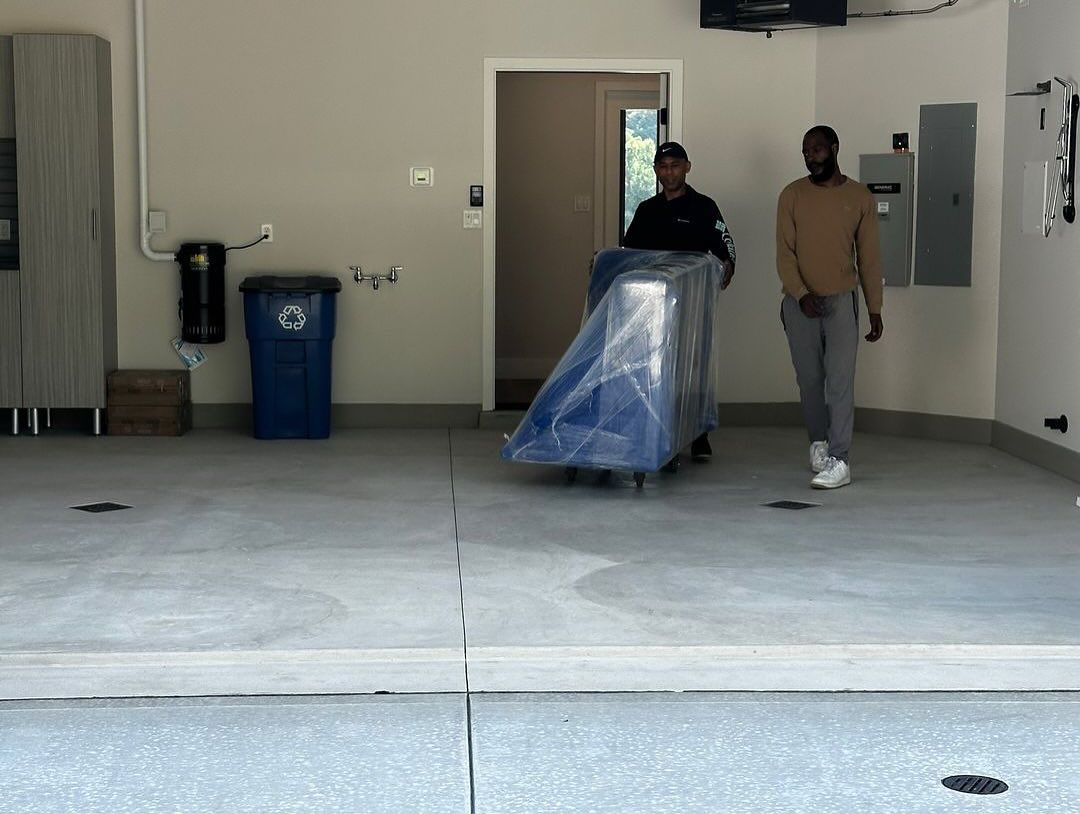 Two people moving a blue-covered object on a dolly in a garage.