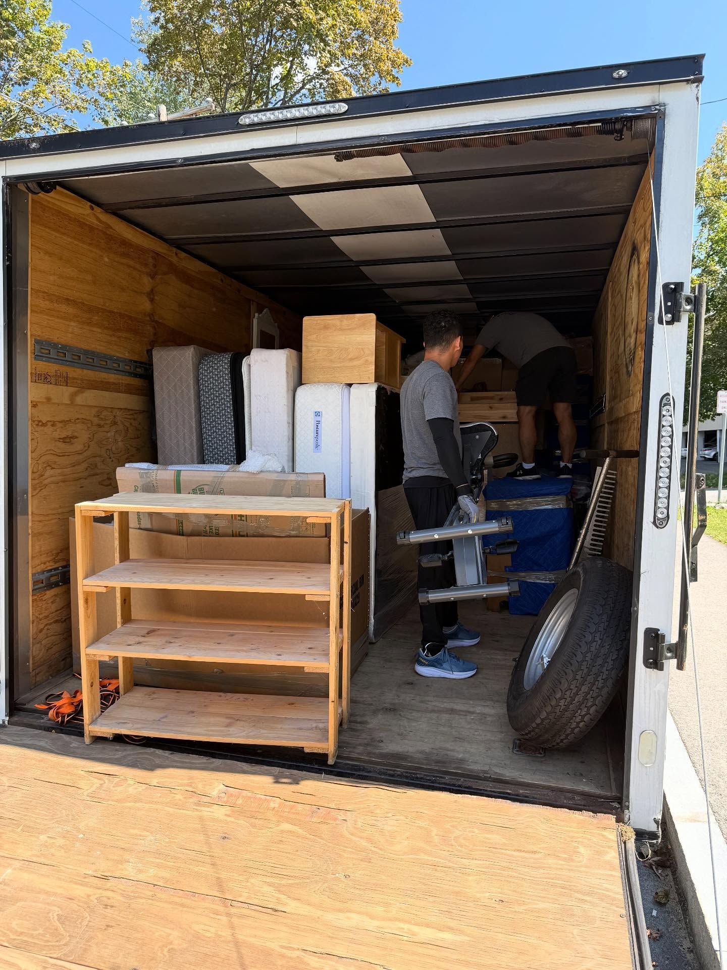 Two people loading furniture and appliances into a moving truck.