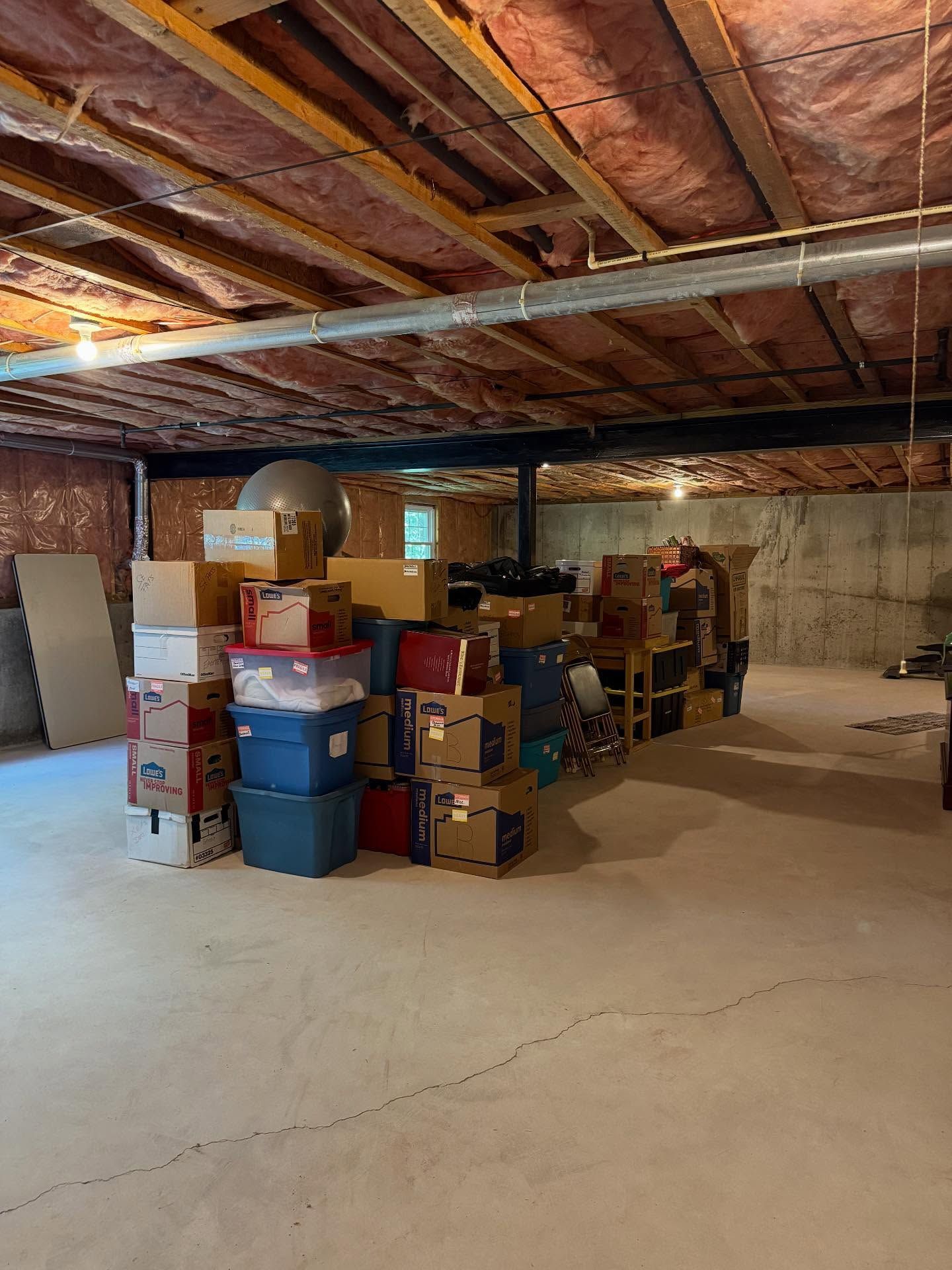 Basement storage area with stacks of cardboard boxes and plastic bins on a concrete floor.