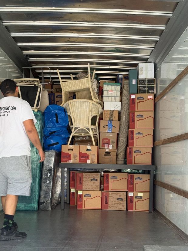 Man loading a moving truck with boxes, furniture, and a rolled rug.