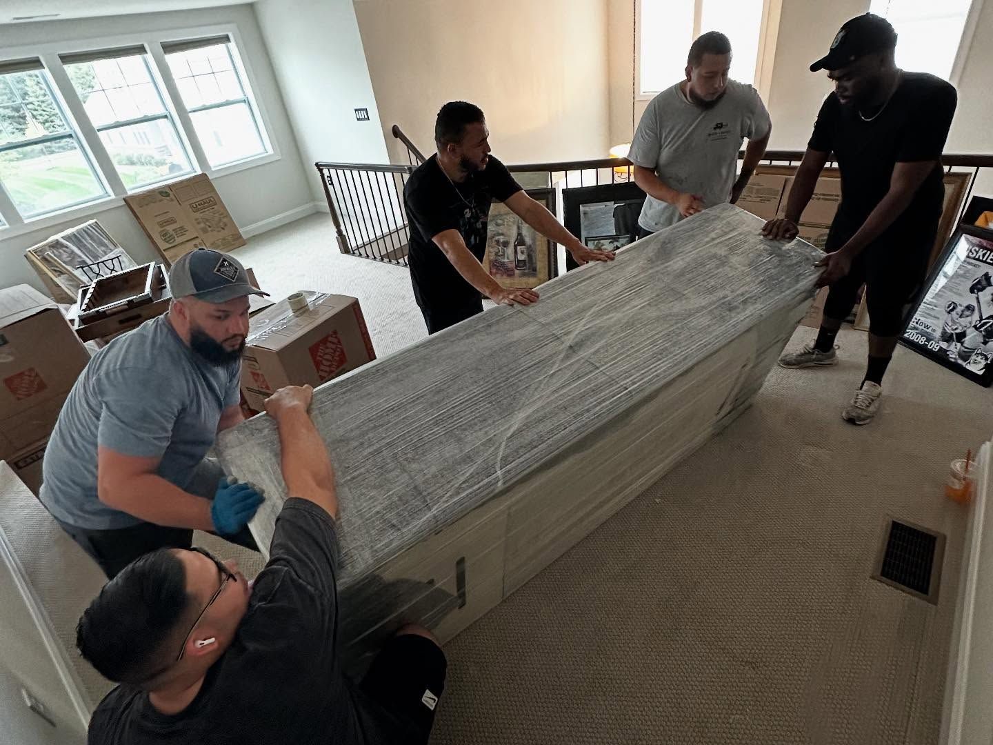 Movers carrying a large, wrapped object up a staircase.