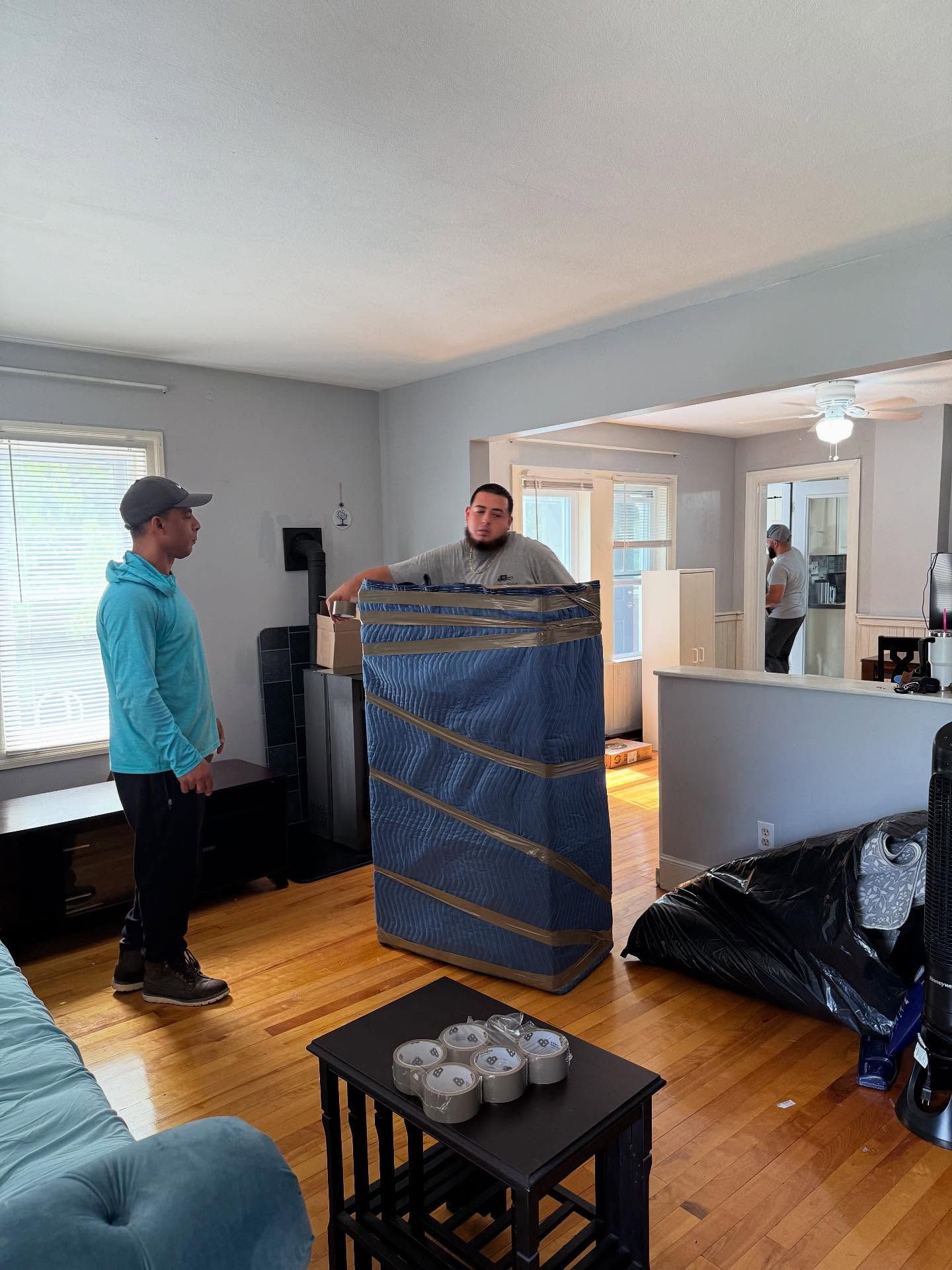 Two movers in a living room, one holding a wrapped item, the other looking on.