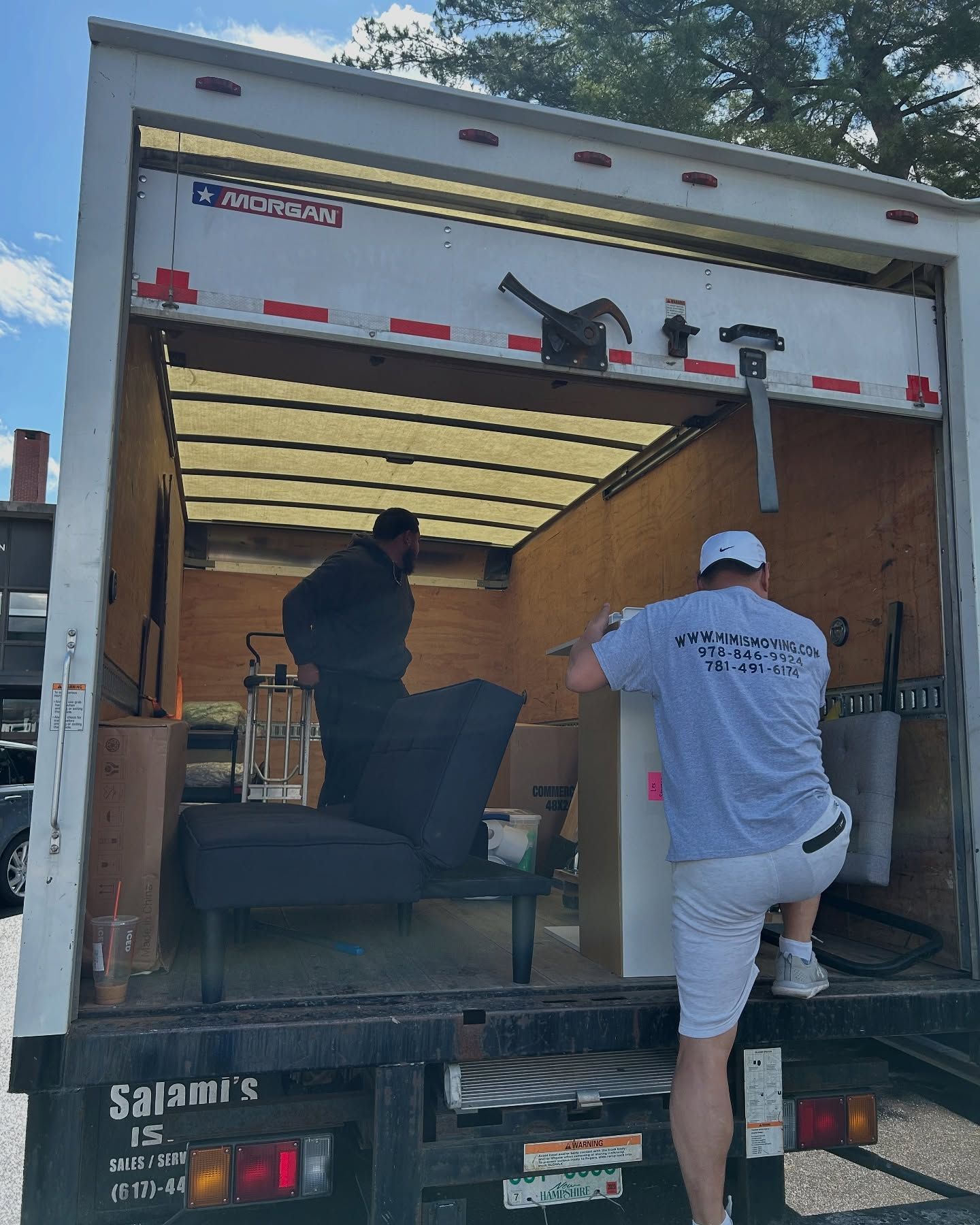 Two people loading a moving truck. One person is in the truck. The other is climbing in.