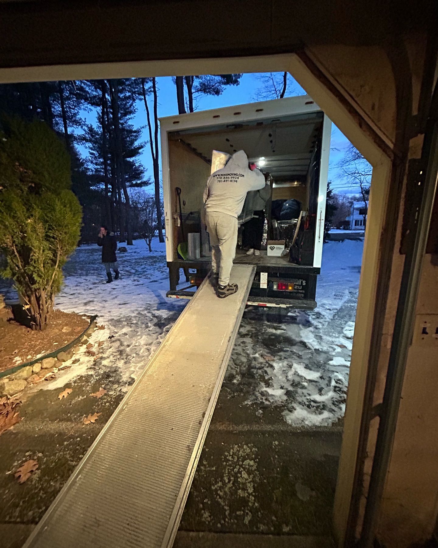 Person loading items into a moving truck from a garage in a snowy environment.
