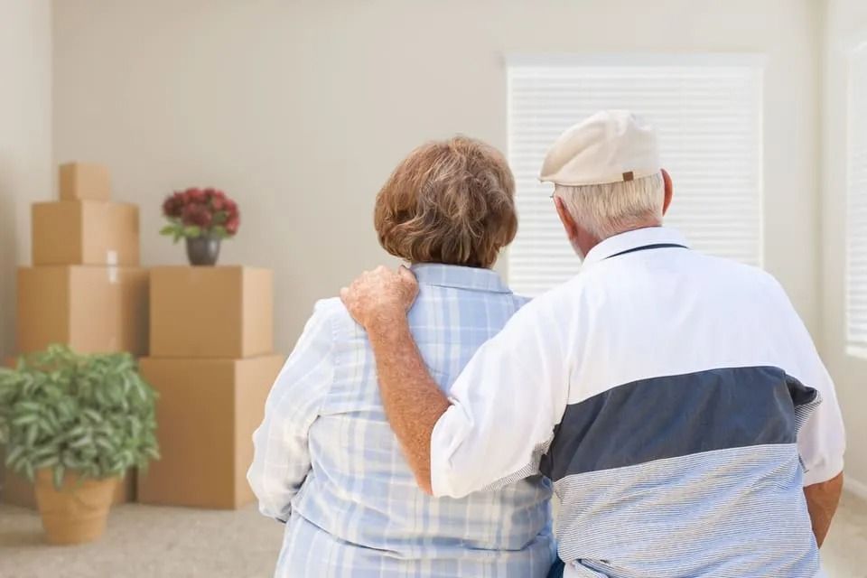 Couple with arm around each other, looking at boxes in empty room, possibly moving.