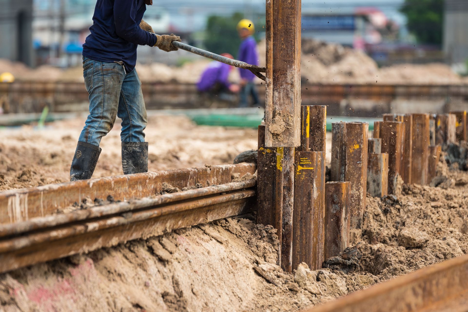 Construction worker using a tool to work on a metal structure in a muddy construction site.