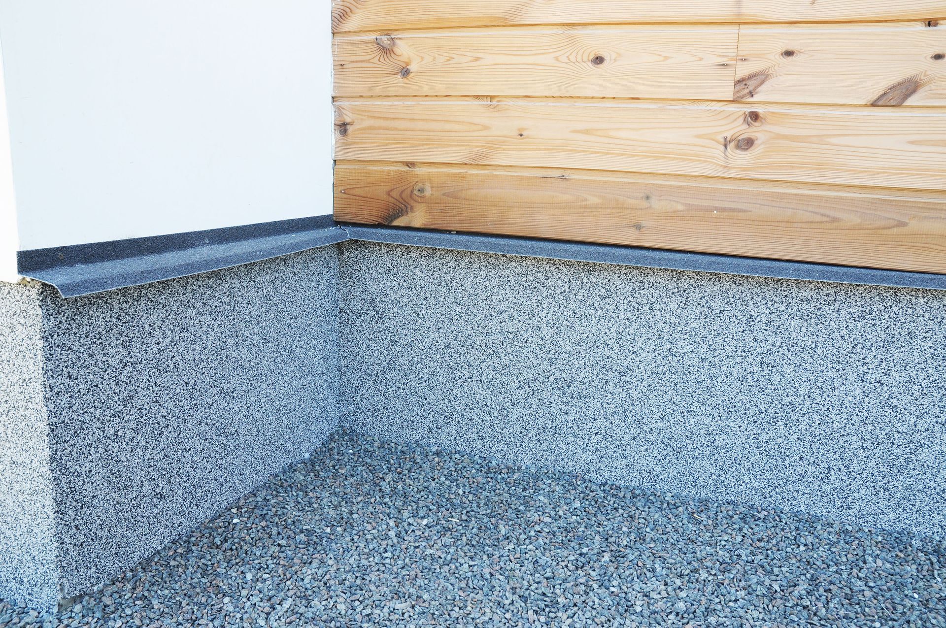 Gray aggregate flooring meets white wall and wood siding.