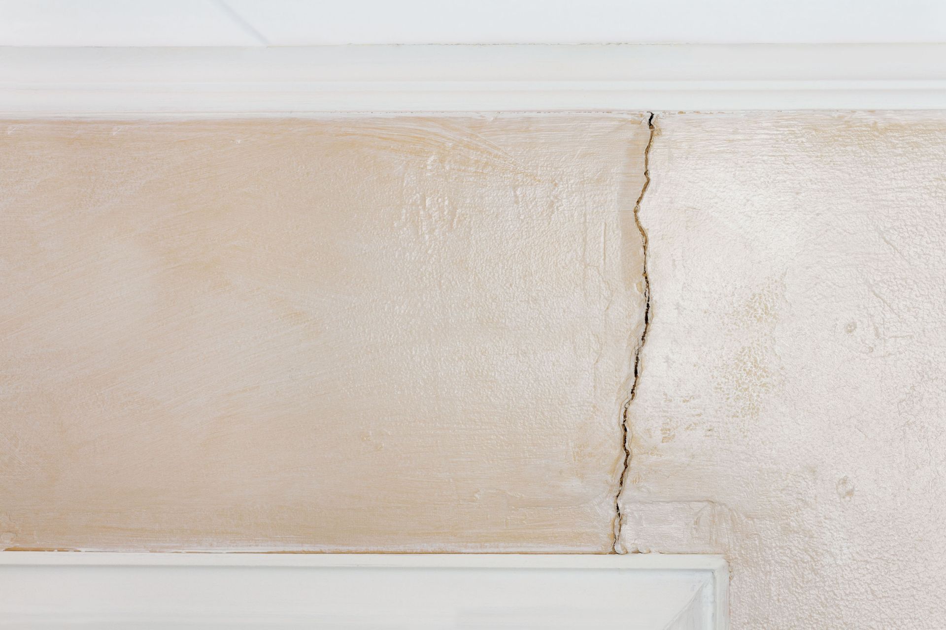 Tan wall with a vertical crack, white molding at top and bottom.