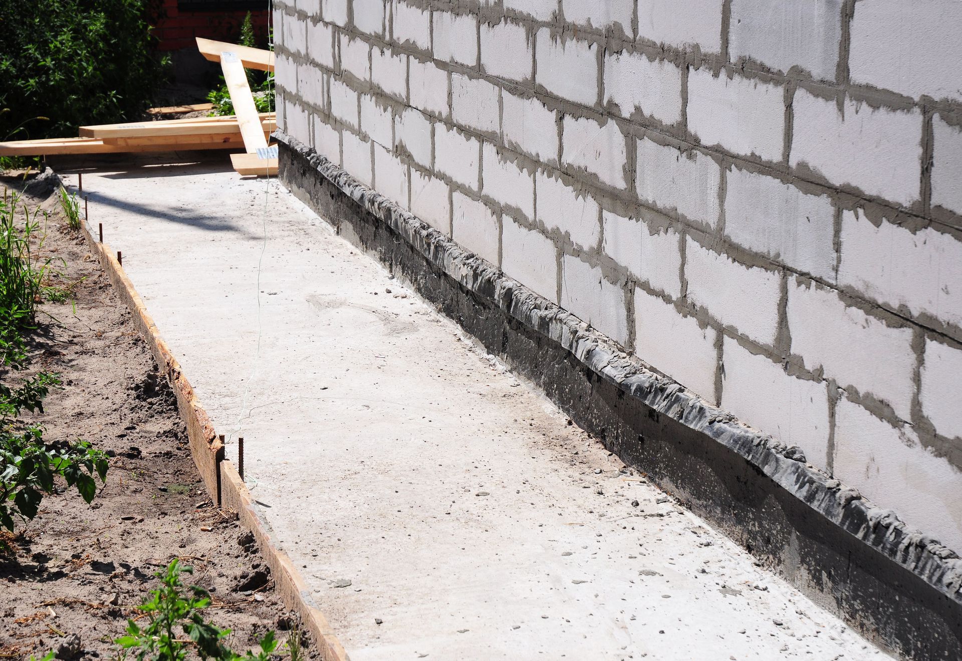Concrete walkway being constructed next to a cinder block wall; wooden forms visible.