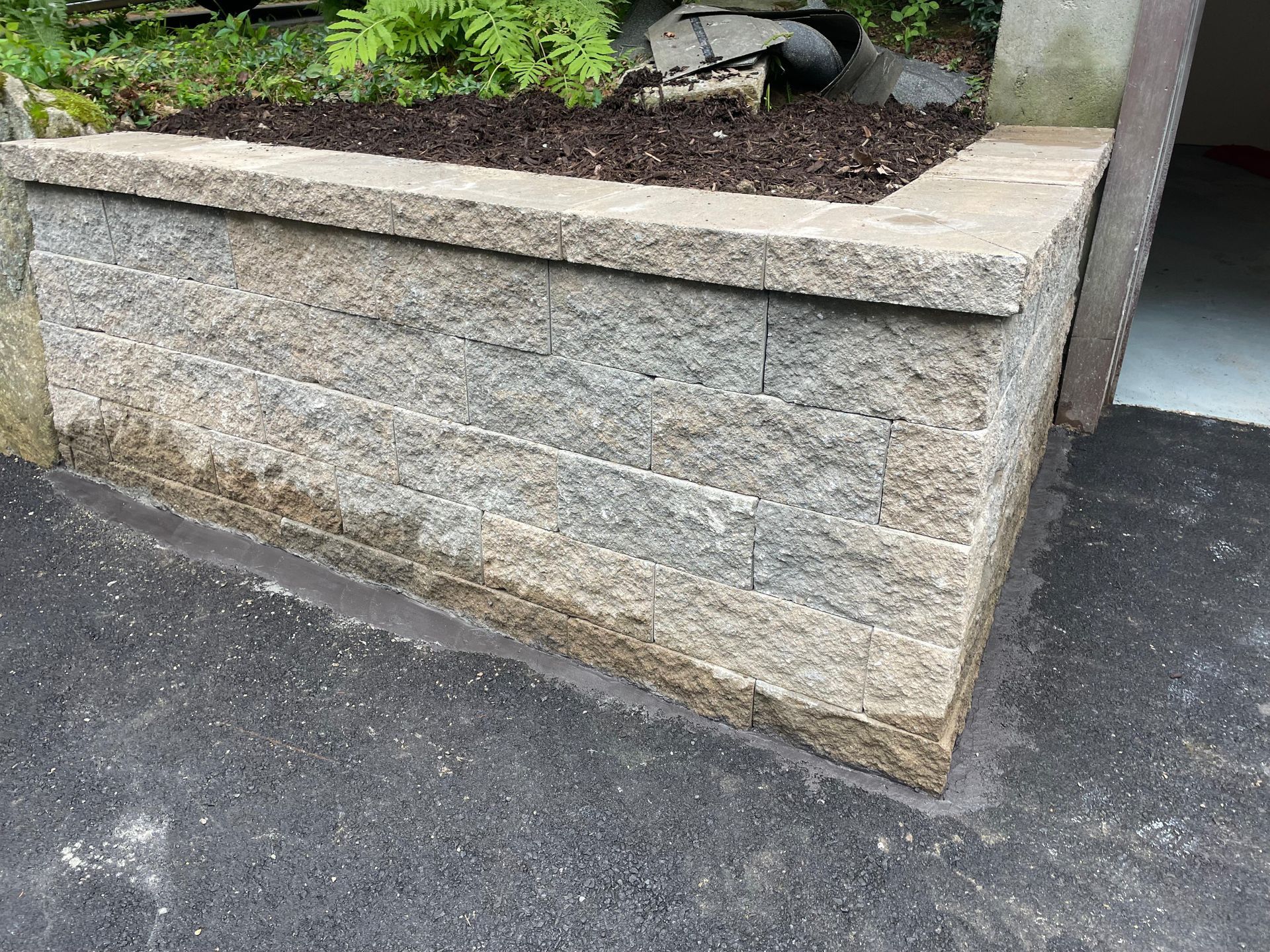 Stone retaining wall with a planter box filled with soil and plants.