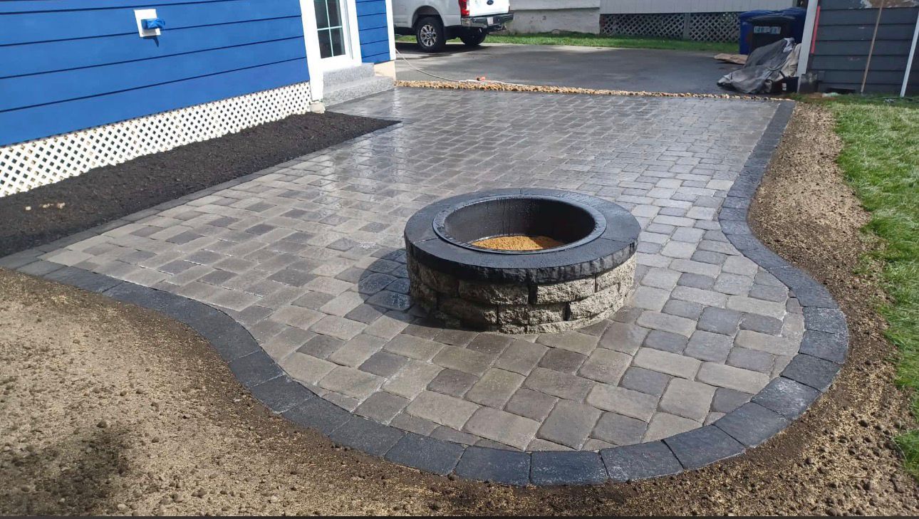 Brick patio with fire pit, blue house, and gravel border.
