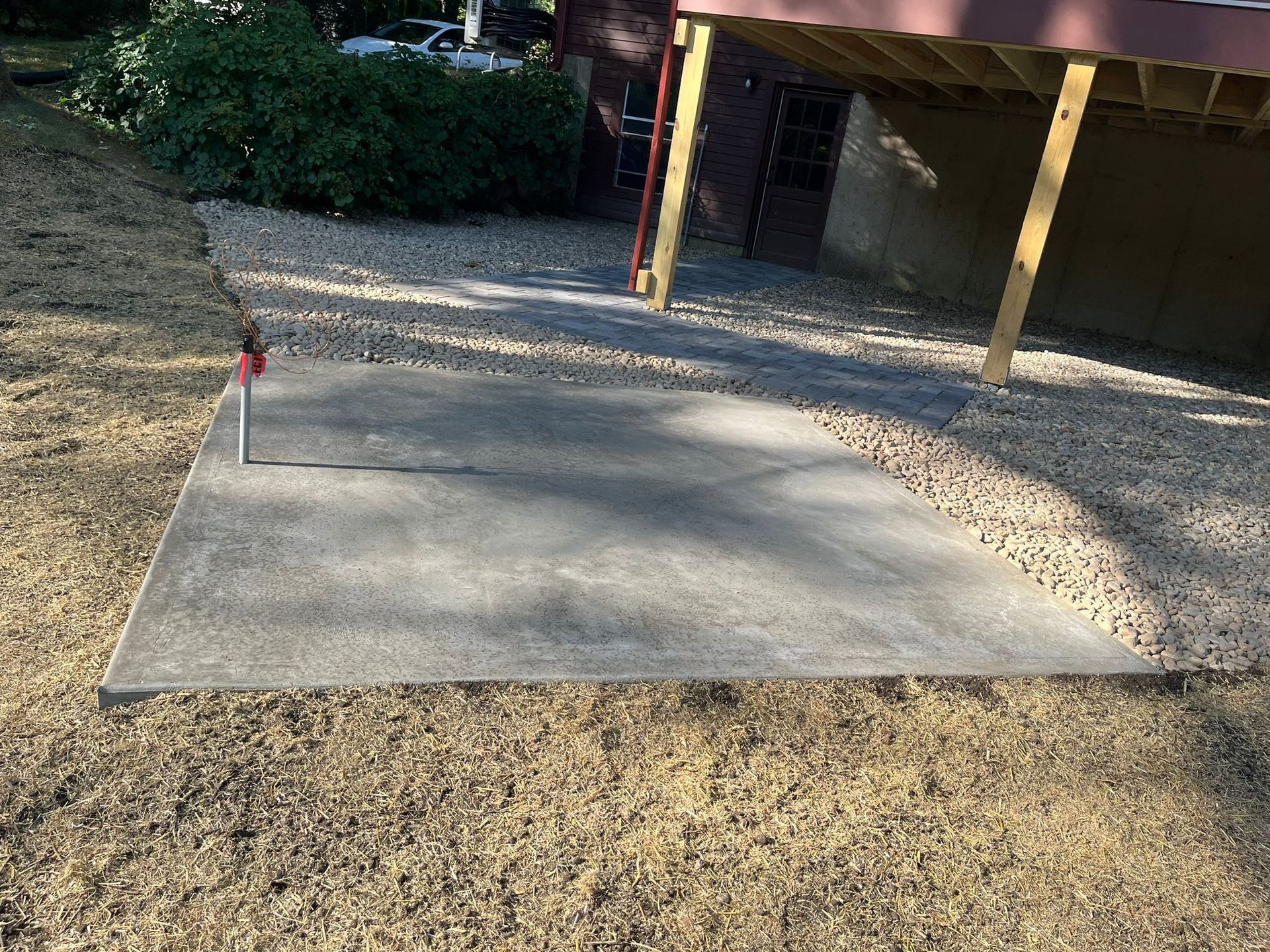 Concrete patio with gravel edging next to a house and deck; grass in foreground.