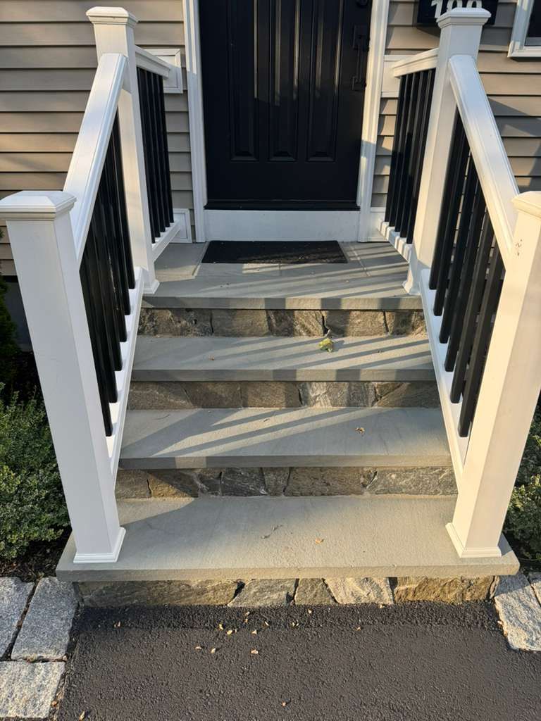 Stone steps leading to a black door with white and black railings.