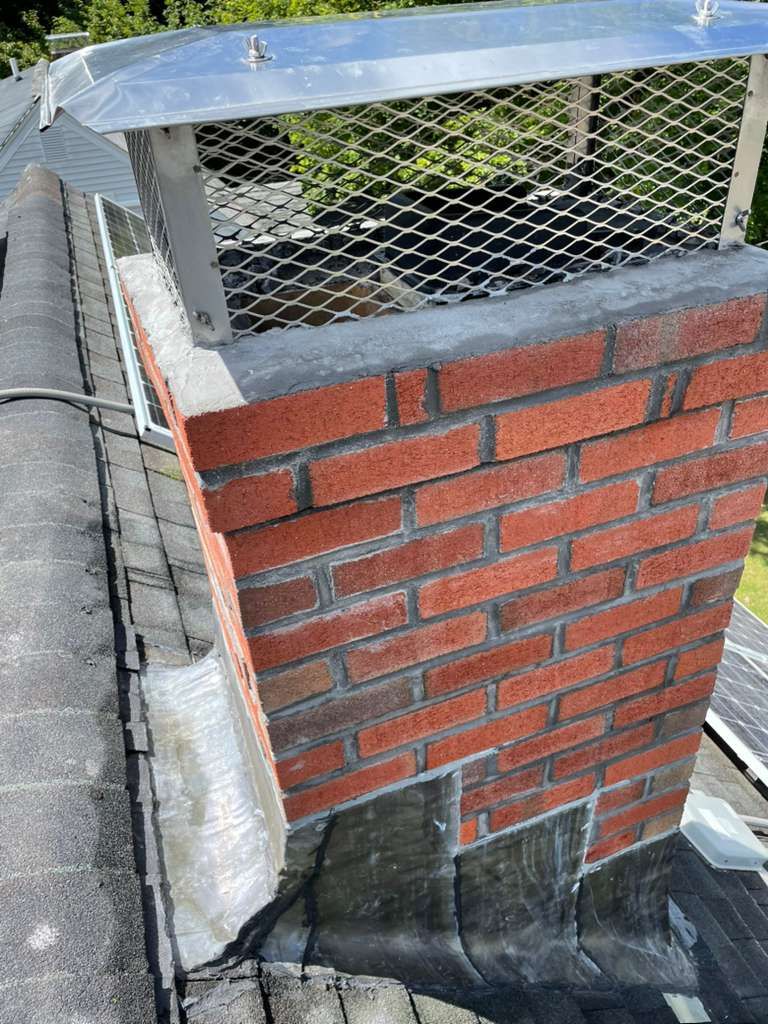 Brick chimney with metal cap on a shingled roof.