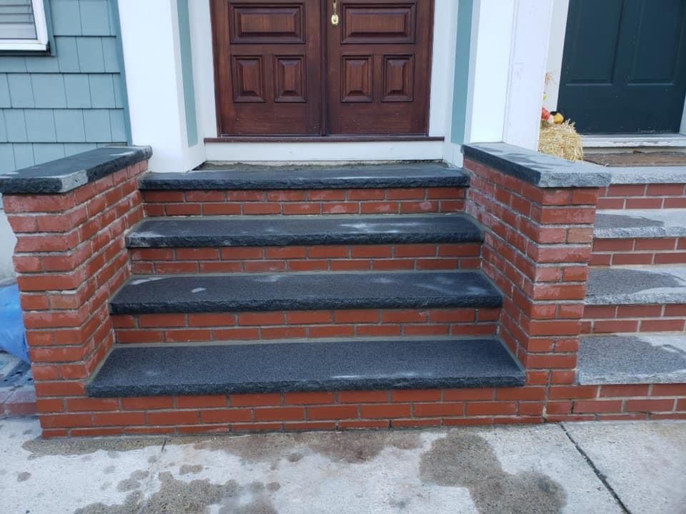 Brick steps leading to a brown door with gray stone treads and red brick risers.