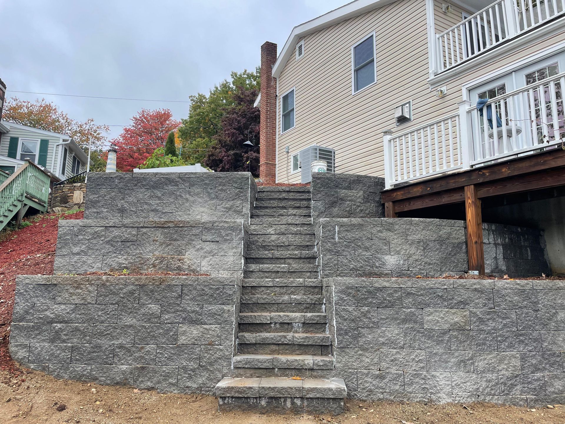 Stone steps ascend through retaining walls, leading to a house with a balcony. Fall foliage visible.