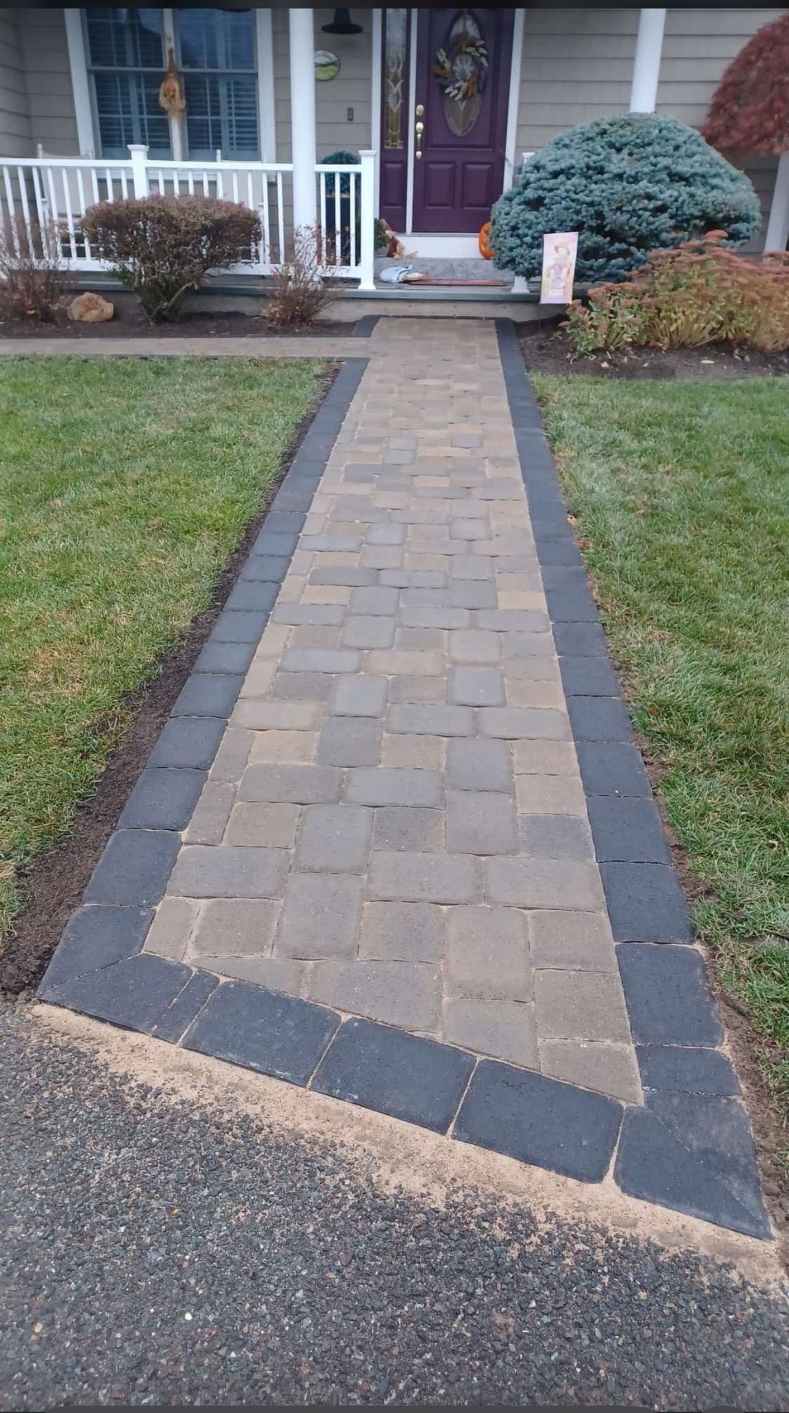 Brick walkway leading to a house with a dark door, bordered by grass.