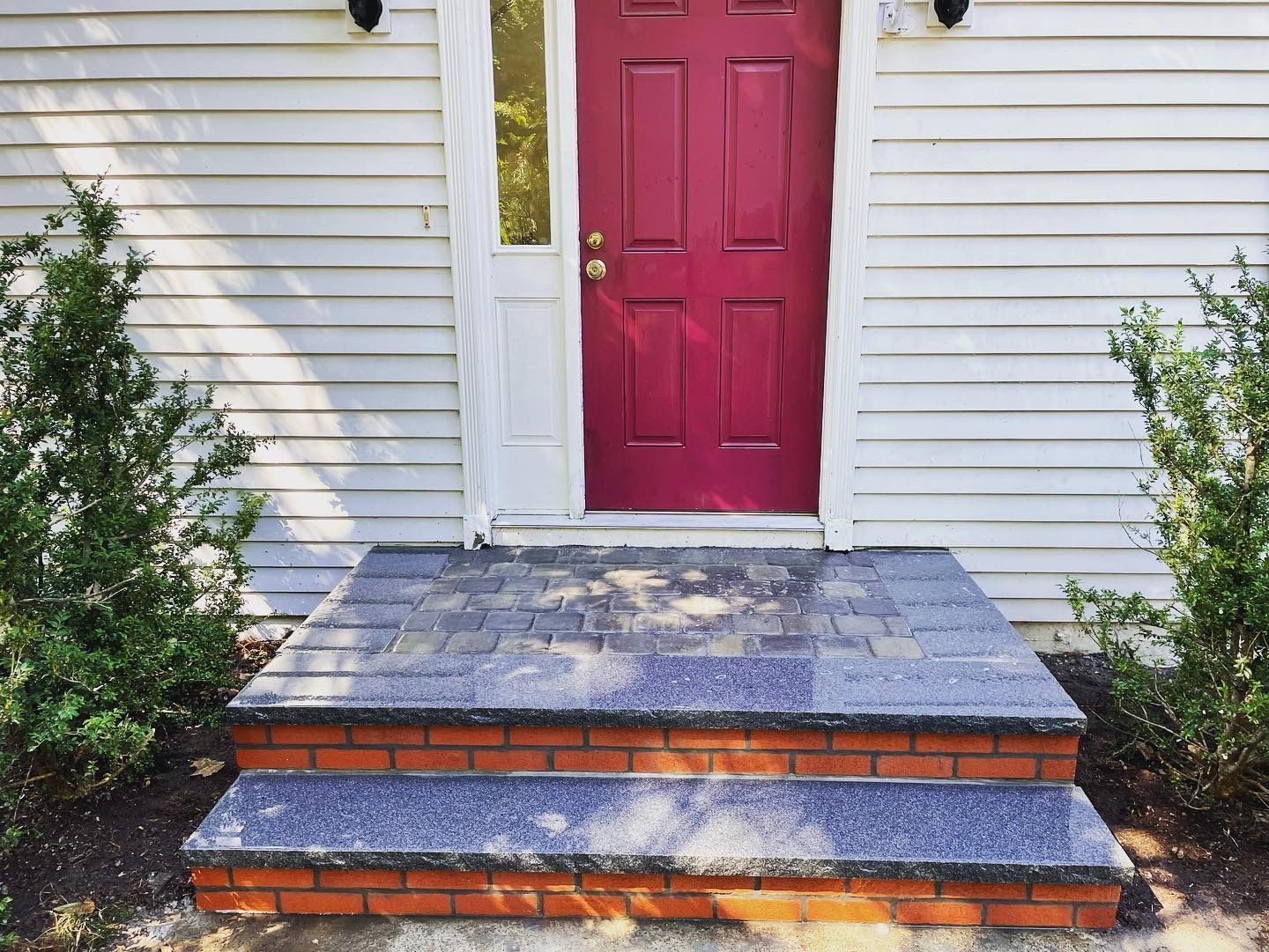 Red door with white trim and steps with a brick base.