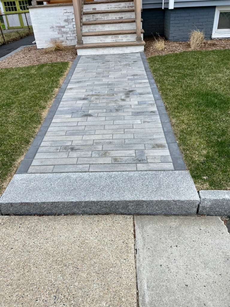 Stone walkway leading to wooden stairs, bordered by green grass.