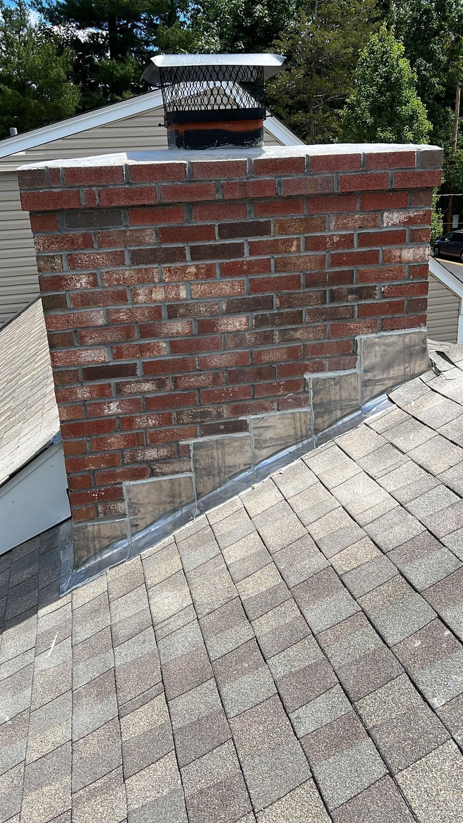 Brick chimney on a shingled roof with flashing, viewed from below.