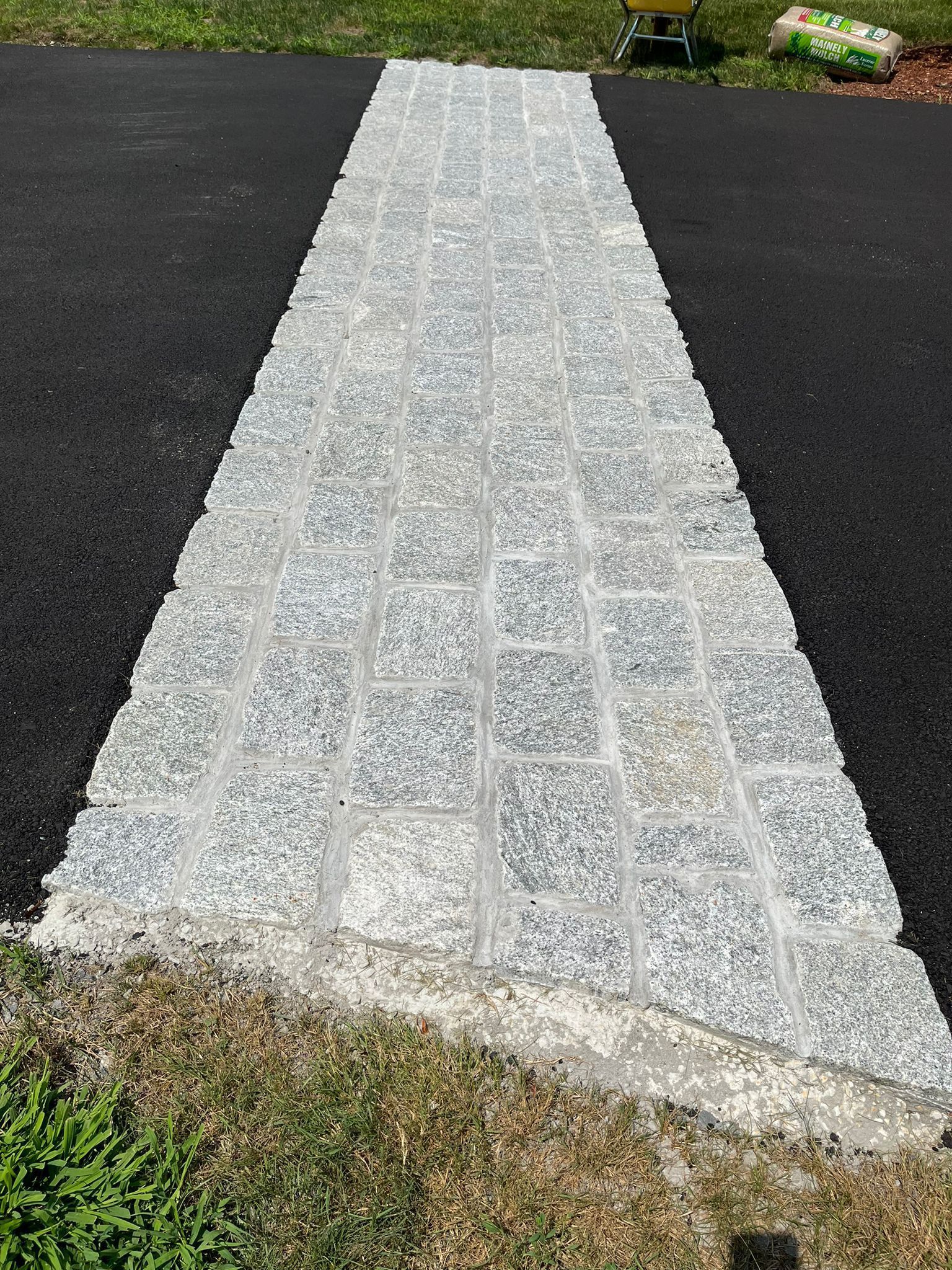 Granite paver walkway laid on asphalt, leading from lawn.