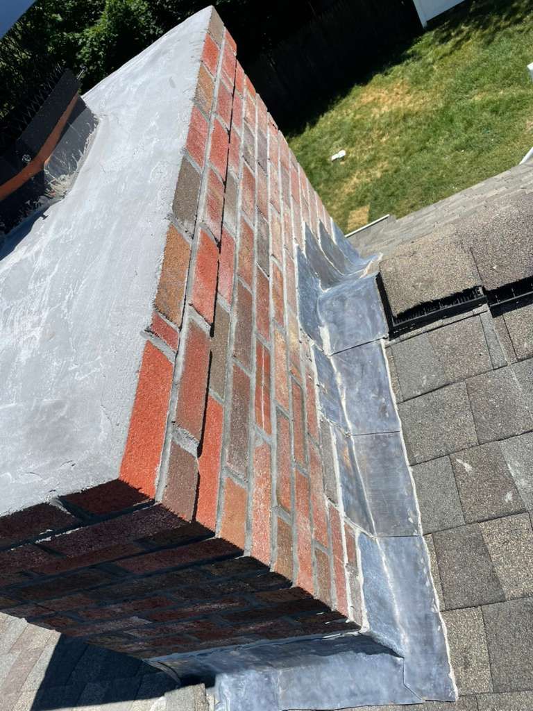 Brick chimney with concrete cap and lead flashing on a shingled roof.