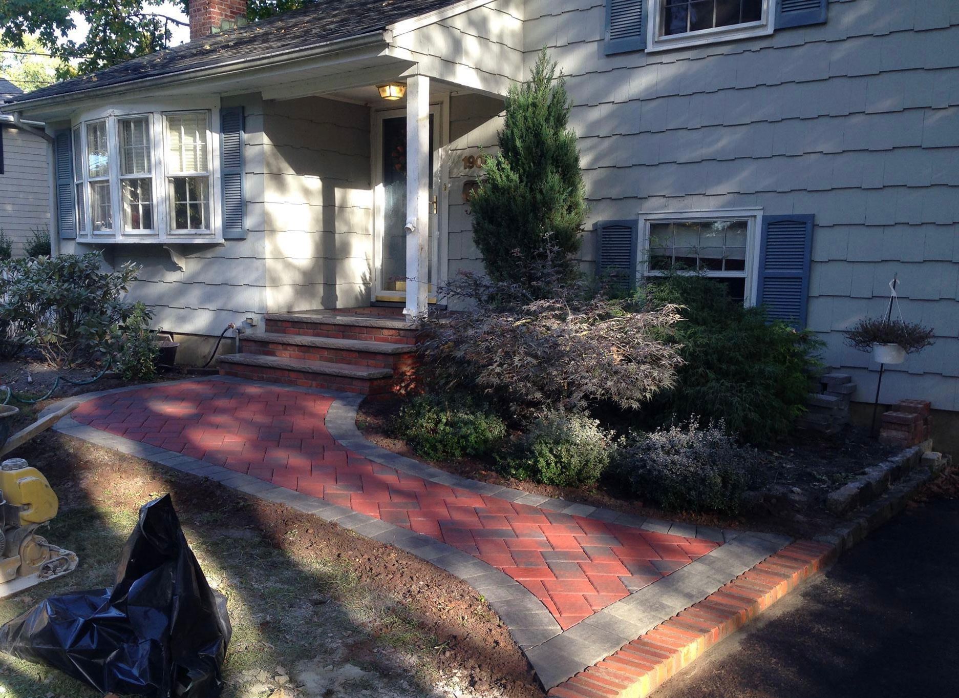 Red brick walkway leading to a house with blue shutters and landscaping.