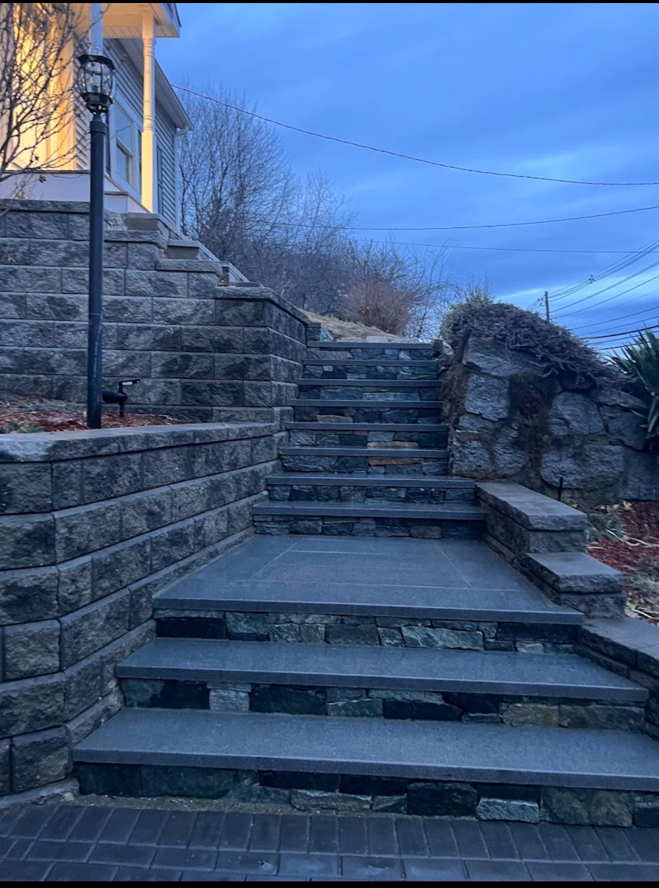 Stone steps leading up to a house; retaining walls flank the steps. Cloudy blue sky.