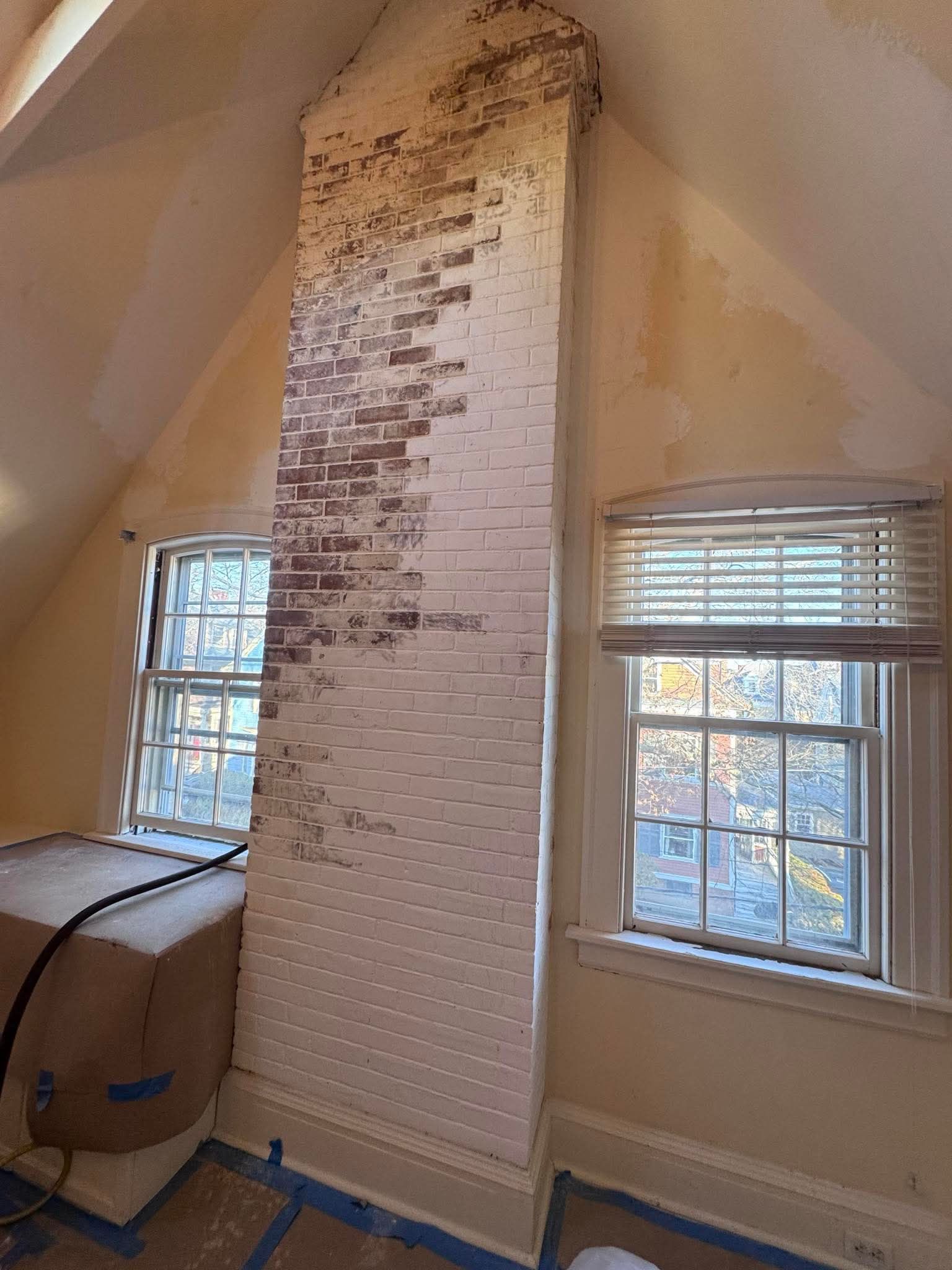 Brick chimney in a room with two windows and sloped ceiling.