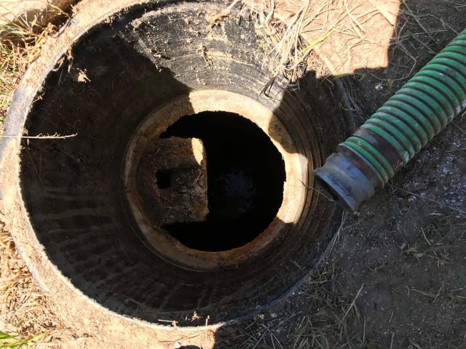 Open manhole with a green hose leading into a dark underground pipe