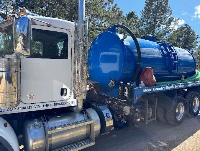 Blue vacuum truck with a large tank parked outdoors among trees