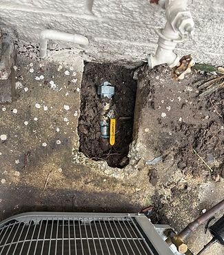 A gas valve is being installed in a hole in the ground next to an air conditioner.