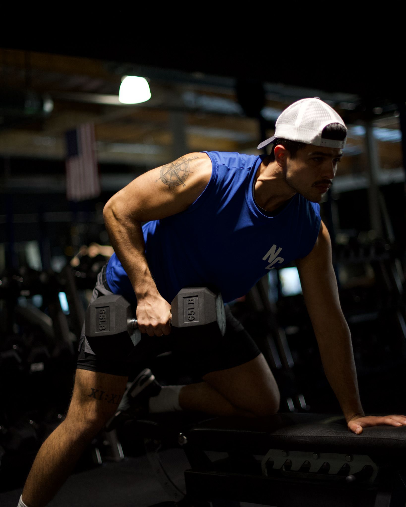 A man is lifting a dumbbell on a bench in a gym.