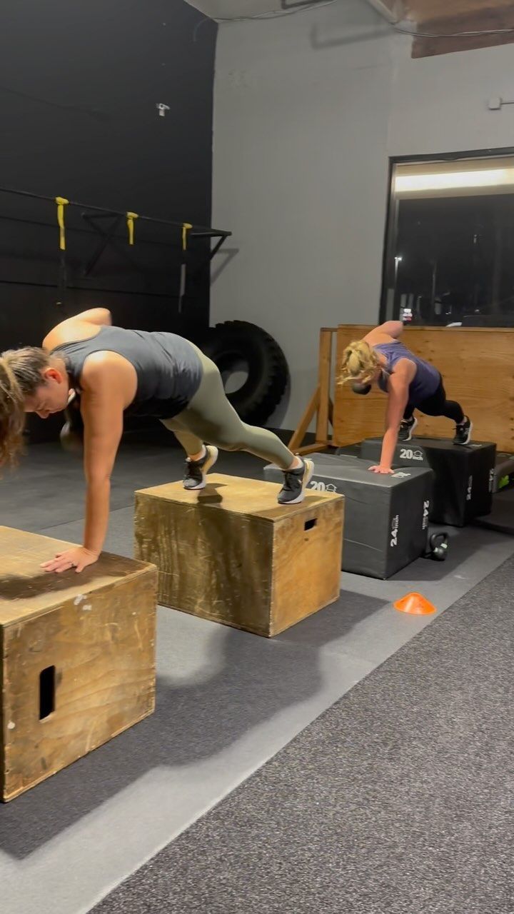 Two women are doing push ups on wooden boxes in a gym.