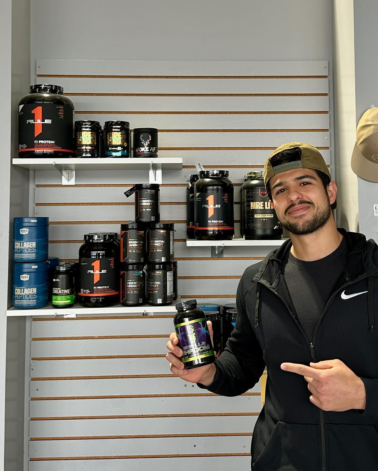 A man is holding a bottle in front of a shelf full of supplements.